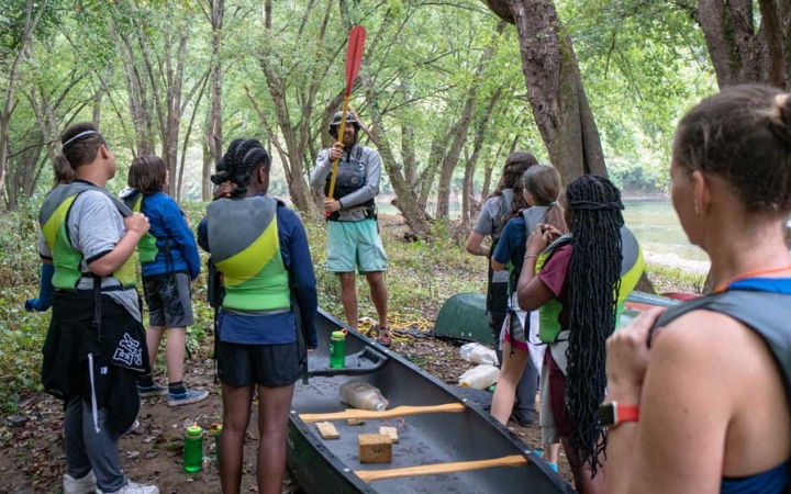 a group of teens listens to an instructor on a canoeing adventure for teens
